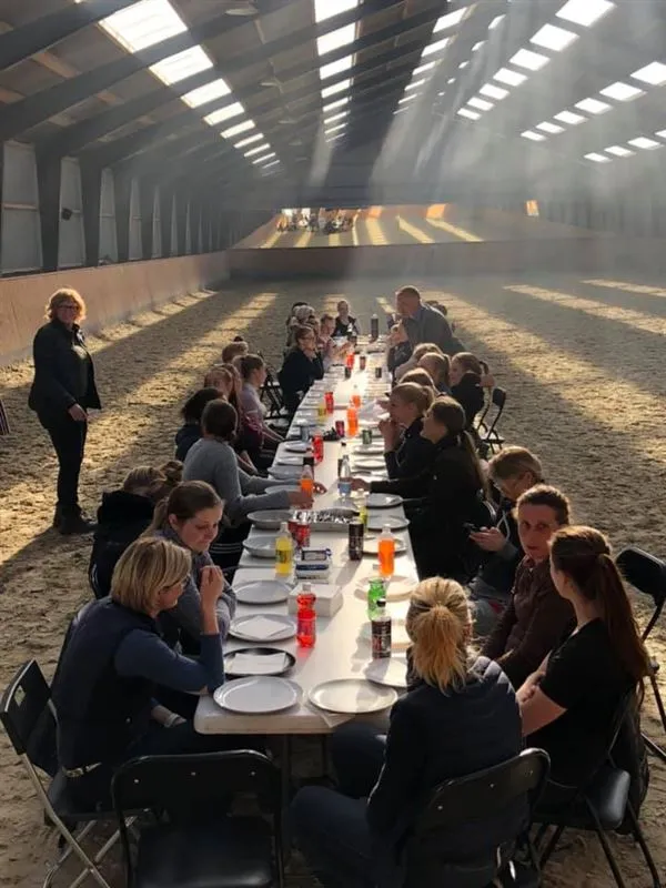 Fællesspisning i ridehallen med mange gæster ved lange borde