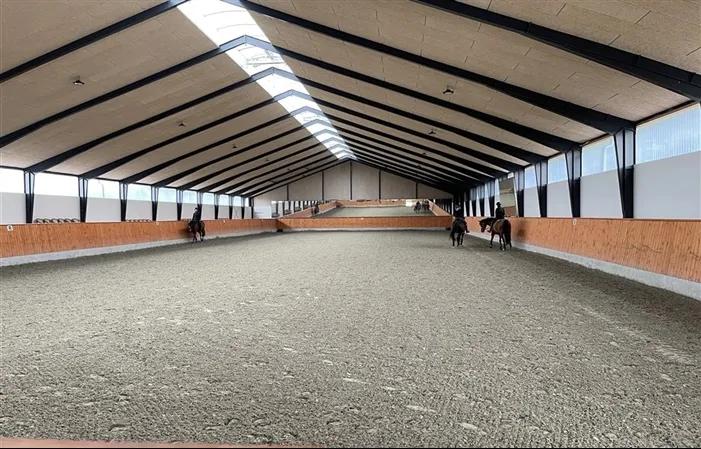 Indendørs ridehal med fiberbund og spejlvæg